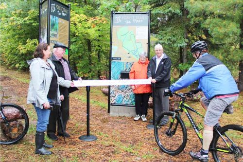 In a slightly different approach to the ribbon-‘cutting’ ceremony, L&A Economic Development Committee member Mike Sewell road through the ribbon held by Addington Highlands Coun. Helen Yanch, Reeve Henry Hogg, Greater Napanee Mayor Marg Isbester and Warden Eric Smith